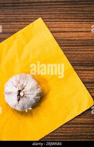 Knoblauchkopf auf einer gelben Serviette und einer traditionellen Holzplatte im Vintage-Stil. Zubereitung eines Rezepts für Knoblauch Kochen. Stockfoto