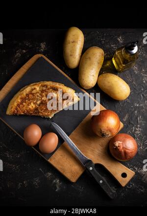 Kartoffelomelett mit seinen Zutaten. Typisch spanisches Gericht, von oben gesehen. Dunkle Küche Stockfoto