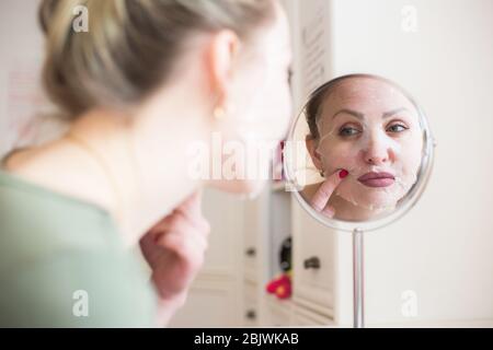 Kosmetische Gesichtsmaske und Mädchen Blick in den Spiegel Stockfoto