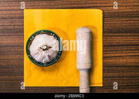 Knoblauchkopf neben einer Hand Mörser auf einer traditionellen Holzplatte. Vorbereitung eines Knoblauchrezeptes für die Herstellung von Aioli. Stockfoto