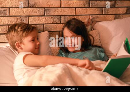 Netter kleiner Bruder und Schwester lesen abends die Schlafenszeit-Geschichte Stockfoto
