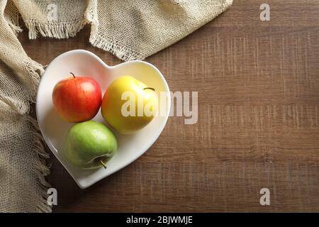 Herzförmiger Teller mit saftigen Äpfeln auf Holztisch, Draufsicht Stockfoto