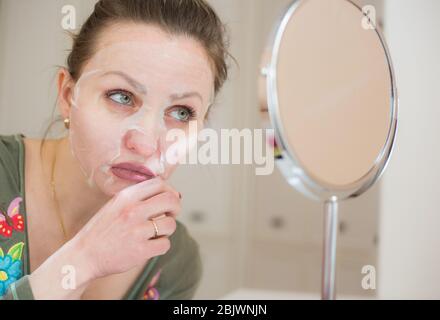 Kosmetische Gesichtsmaske und Mädchen Blick in den Spiegel Stockfoto