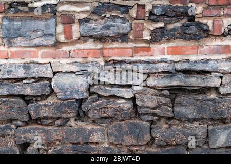 Das alte Steinfundament eines Gebäudes ist über dem Boden freigelegt, mit neueren Ziegeln und Mörtel, die auf die Struktur aufgepfropft wurden. Stockfoto