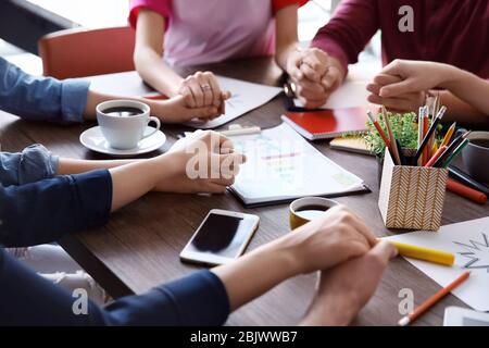 Junge Menschen halten sich die Hände, während sie an einem Projekt arbeiten. Einheitlichkeit Stockfoto