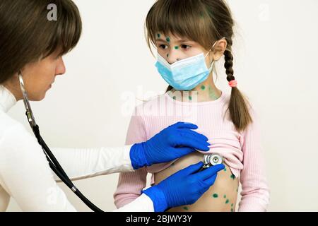 Arzt untersucht Mädchen mit grünen Ausschlägen auf Gesicht und Bauch erkrankt an Windpocken, Masern oder Röteln Virus. Stockfoto