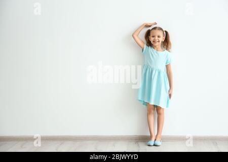 Kleines Mädchen misst Höhe in der Nähe von Lichtwand Stockfoto