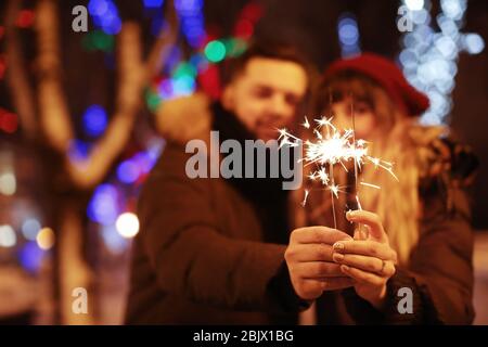 Junge liebevolle Paar hält Sparklers im Freien am Winterabend Stockfoto