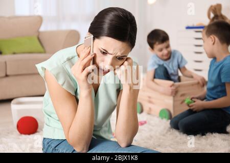 Verärgerte Kindermädchen am Telefon, während zwei kleine Jungen zu Hause spielen Stockfoto