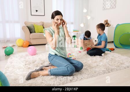 Müde Kindermädchen am Telefon reden, während zwei kleine Jungen zu Hause spielen Stockfoto