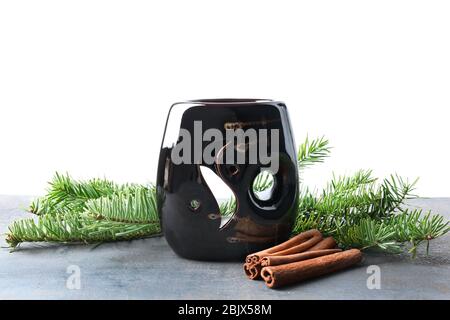 Duftlampe mit Tannenzweigen und Zimtstangen auf Tisch vor weißem Hintergrund Stockfoto