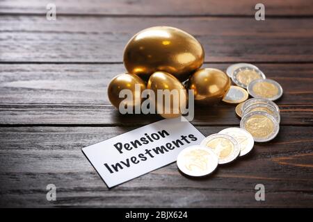 Goldene Eier, Münzen und Schilder RENTEN INVESTITIONEN auf Holzhintergrund Stockfoto