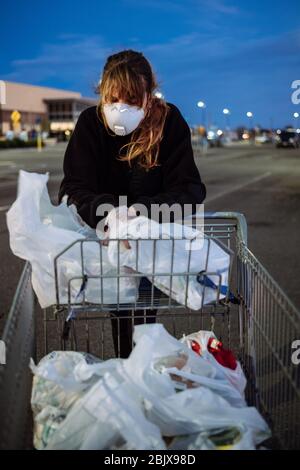 Eine Frau, die während der weltweiten Pandemie Covid-19 eine PSA-Gesichtsmaske und Handschuhe vor einem Lebensmittelgeschäft trägt. Stockfoto