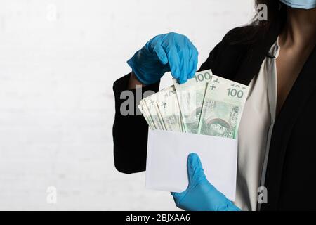 Die Frau schiebt ein Bündel von hundert polnischen Zloty-Banknoten in einen weißen Umschlag. Stockfoto