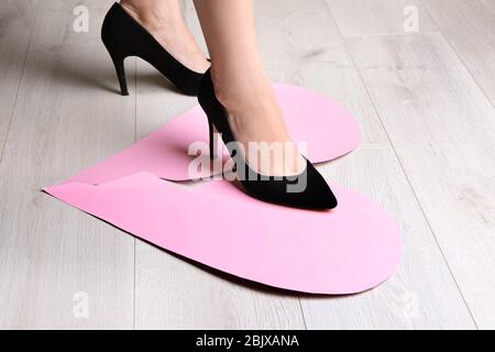 Frau tritt auf gebrochenes Papierherz auf den Boden. Beziehungsprobleme Stockfoto