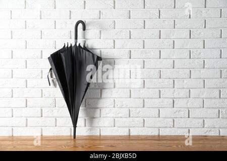 Schwarzer Schirm in der Nähe von Ziegelwand Stockfoto