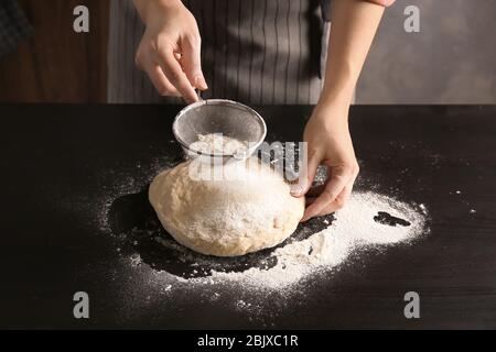 Junge Frau, die Mehl über Teig auf dem Tisch sieben Stockfoto