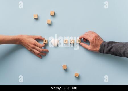 Männliche und weibliche Hand machen ein I love you Zeichen geschrieben auf Holzblöcken mit Herz-förmigen Marmor in der Mitte. Stockfoto