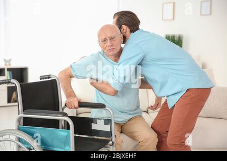 Junge Pflegekraft hilft älteren Mann, im Rollstuhl zu Hause sitzen Stockfoto