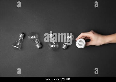 Frau hält Leuchtstofflampe in der Nähe Glühlampen auf dunklem Hintergrund Stockfoto