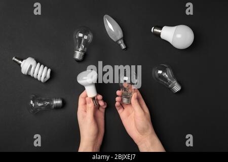 Frau, die LED und Glühlampe in der Nähe verschiedener Glühlampen auf dunklem Hintergrund hält Stockfoto
