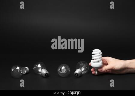 Frau hält Leuchtstofflampe in der Nähe Glühlampen auf dunklem Hintergrund Stockfoto