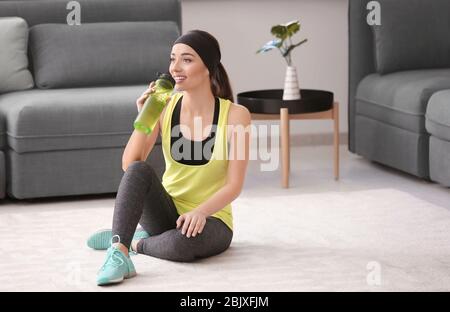 Schöne junge Frau, die Wasser trinkt, nachdem sie Fitness-Übungen zu Hause gemacht hat Stockfoto