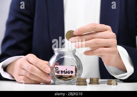 Frau, die Münze in Glas mit dem Etikett "PENSION" auf dem Tisch legt Stockfoto