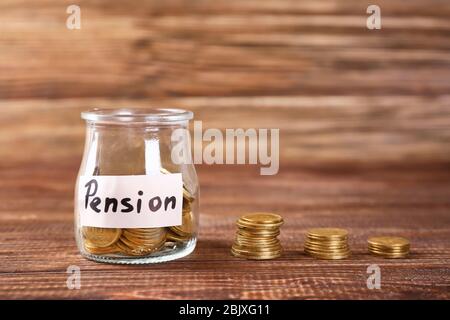 Glas mit Etikett "PENSION" und Münzen auf Holztisch Stockfoto