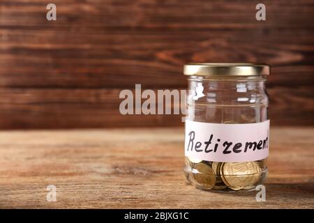 Glas mit Etikett "RETIREMENT" und Münzen auf Holztisch. Pensionsplanung Stockfoto