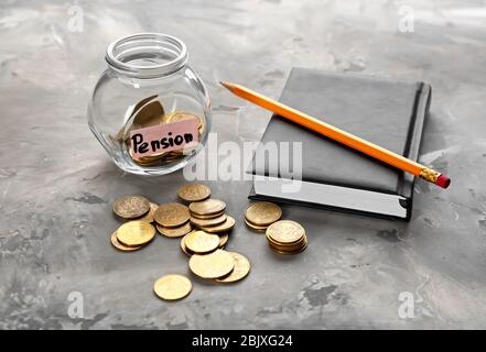 Münzen im Glasgefäß mit Etikett "PENSION" und Notizbuch auf dem Tisch Stockfoto