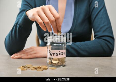 Frau, die Münze in Glas mit dem Etikett "PENSION" auf dem Tisch legt Stockfoto