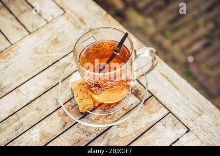 Tee in Glas Tasse auf einem Holztisch draußen im Garten. Teelöffel und Keks. Gesunde Lebensweise. Hintergrund. Holzmuster. Stockfoto