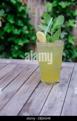 Frische hausgemachte Limonade im Glas mit Zitronenscheibe, Minzblättern, Eiswürfeln und Stroh. Auf Holztisch, im Garten. Sommerdrink. Stockfoto