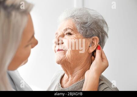 Otolaryngologist das Hörgerät im Ohr des älteren Frau auf hellen Hintergrund Stockfoto