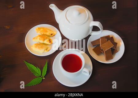 Weiße Porzellan Teekanne, Teebecher mit Tee und Süßigkeiten auf einem dunklen Holztisch. Stockfoto