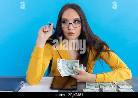 Beim Zählen von Geld verwendet eine junge Frau einen Rechner und ein Tablet, um die Börse zu überprüfen. Stockfoto