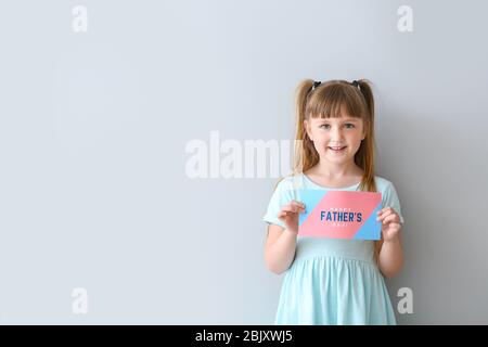 Süße kleine Mädchen mit Grußkarte für Vatertag auf hellen Hintergrund Stockfoto