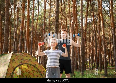 Vater und sein kleiner Sohn Training mit Hanteln in der Nähe von Camping Zelt im Wald Stockfoto