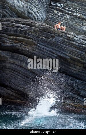 Teenager-Junge sieht seinen Freund springen von der Klippe ins Wasser, Manarola, Cinque Terre, Italien, Europa Stockfoto