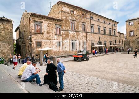 Priester auf langen schwarzen Gewand spricht mit den einheimischen Männern auf den Stufen der Kirche San Donato auf dem Hauptplatz von Cività di Bagnoregio, Civita Bagno, eine alte Stockfoto