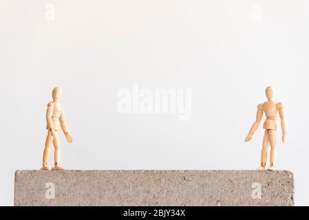 Soziale Distanzierung Symbol: Zwei hölzerne menschliche Figuren stehen auf einem Betonblock mit einer guten Trennung zwischen ihnen. Stockfoto