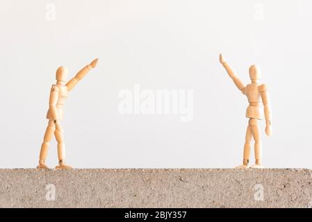 Soziale Distanzierung Symbol: Zwei hölzerne menschliche Figuren stehen auf einem Betonblock mit einer guten Trennung zwischen ihnen, winken Stockfoto