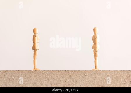 Soziale Distanzierung Symbol: Zwei hölzerne menschliche Figuren stehen auf einem Betonblock Blick auf einander mit einer guten Trennung zwischen ihnen. Stockfoto