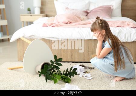 Kleines Mädchen in Zimmer mit überschnittenen Zimmerpflanze und Papier Stücke auf dem Teppich Stockfoto