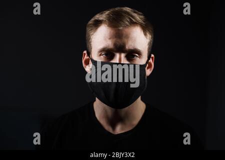 Schöner Mann in schwarzem T-Shirt tragen schwarze medizinische Maske, grauer Hintergrund. Coronavirus Covid-19 Quarantänezeitkonzept Stockfoto