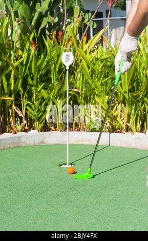 Mann, der einen Mini-Golf Putt mit Latexhandschuhen in der Sonne Stockfoto