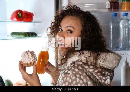 Angst Frau im Akt des Essens leckere Kuchen in der Nähe von Kühlschrank bei Nacht gefangen Stockfoto