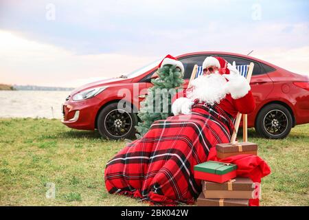 Weihnachtsmann mit Geschenken und Tannenbaum Musik hören in der Nähe von Auto auf Riverside Stockfoto
