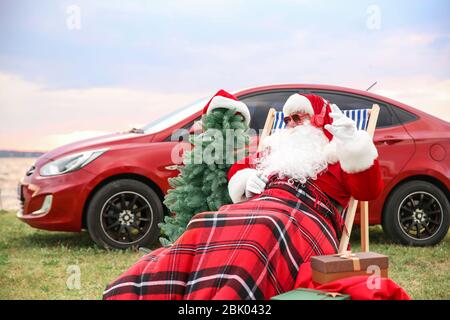 Weihnachtsmann mit Geschenken und Tannenbaum Musik hören in der Nähe von Auto auf Riverside Stockfoto
